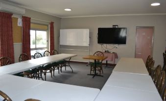 a room with multiple tables and chairs , a large screen on the wall , and windows at Colac Mid City Motor Inn