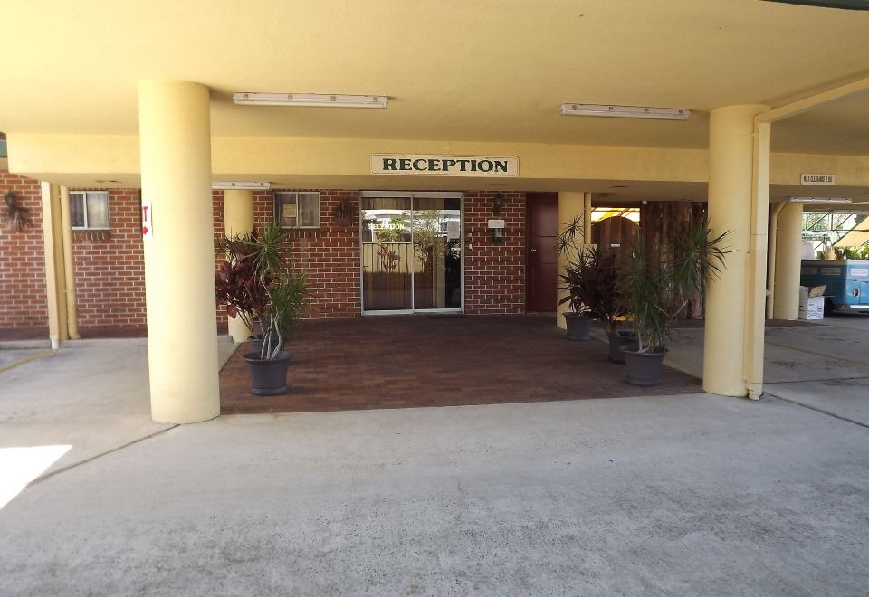 a brick building with an open door , a reception area , and several potted plants in front of it at The Mullum Motel