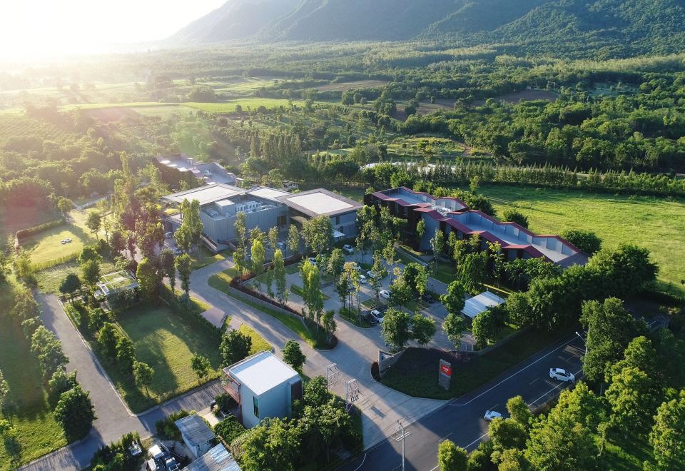 aerial view of a modern building complex surrounded by greenery and mountains , with the sun setting in the background at Dusitd2 Khao Yai