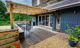 a wooden deck with a wooden pergola , dining table , and chairs , surrounded by greenery and flowers at Dunraven Hotel