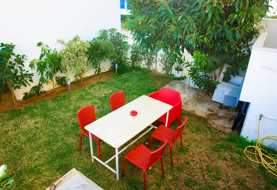 a white table with red chairs is surrounded by a lush green garden in front of a house at The View Gammarth