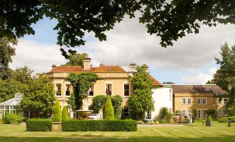 a large , two - story house with a red roof and white walls , surrounded by greenery and trees at Woodland Manor Hotel