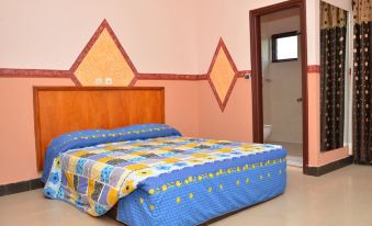 a cozy bedroom with a blue bedspread , yellow and white pillows , and a wooden headboard at Hotel International