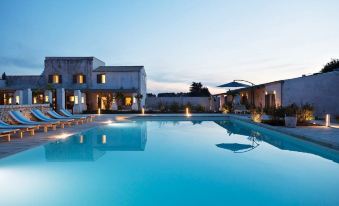 a large swimming pool is surrounded by a white building and lounge chairs , with the sky above at Borgo Sentinella