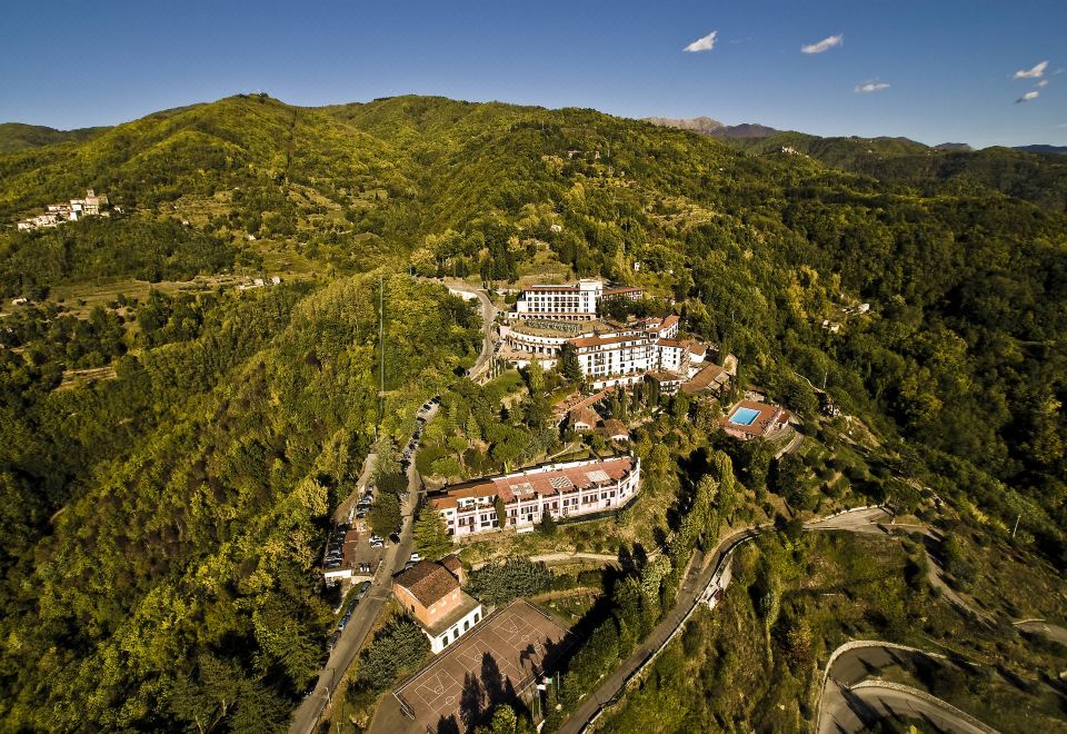 aerial view of a large white building surrounded by trees and mountains , located in a mountainous area at Renaissance Tuscany Il Ciocco Resort & Spa
