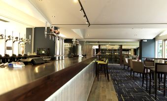 a modern restaurant with a long wooden bar , several dining tables , and a large window at Crowne Plaza Stratford Upon Avon