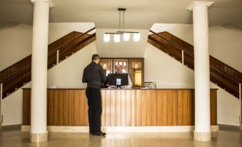 a man standing at a hotel reception desk , surrounded by wooden paneling and a chandelier at Hotel Novo