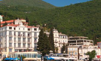 a picturesque coastal town with a hotel situated on the waterfront , surrounded by lush greenery and mountains in the background at Hotel Savoy