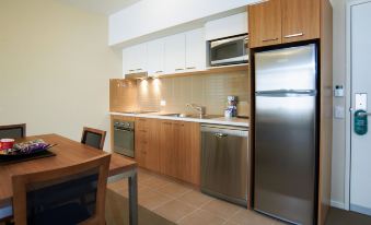 a kitchen with wooden cabinets , stainless steel appliances , and a dining table in the background at Quest Bendigo Central
