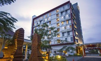 a modern hotel building with a white exterior and large windows , situated next to a tree - lined street at Metland Hotel Cirebon by Horison
