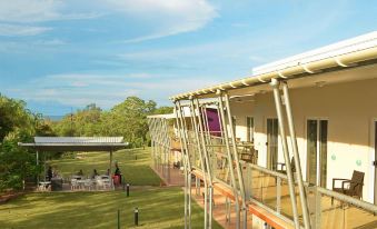 a large building with a glass exterior and balconies is surrounded by grass and trees at Club Tropical Resort Darwin