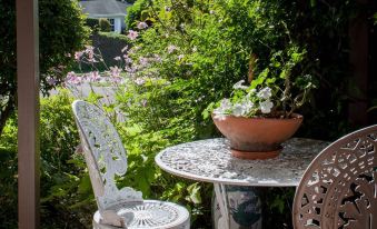 a white metal table and chairs set on a porch , surrounded by lush greenery and a view of a garden at The Loft Bed and Breakfast