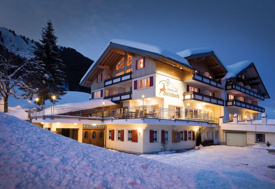 a large white building with a red roof is situated in the middle of snow - covered mountains at Hotel Steinbock