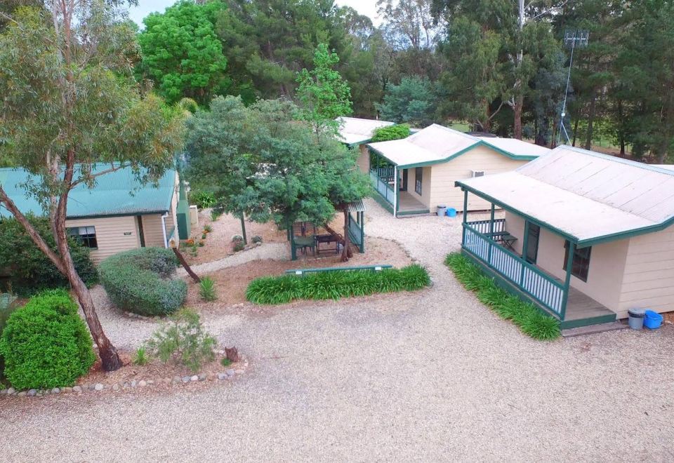 aerial view of a small house surrounded by trees and bushes , with a pool in the foreground at Fernleigh Accommodation