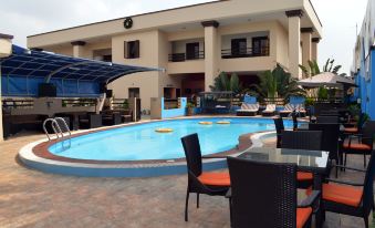 a large swimming pool with a white building and blue umbrellas in the background , surrounded by tables and chairs at De Santos Hotel