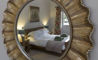 a large , round mirror with a gold frame is reflecting a bedroom 's bed and nightstand at The Horseshoe Country Inn