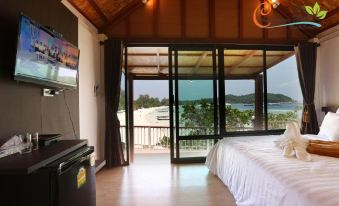 a bedroom with a bed , television , and sliding glass doors leading to a balcony overlooking the ocean at Chareena Hill Beach Resort