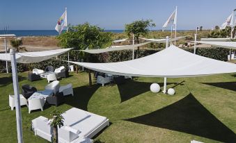 a large white tent is set up in a grassy area near the ocean , with lounge chairs and umbrellas nearby at DoubleTree by Hilton Islantilla Beach Golf Resort