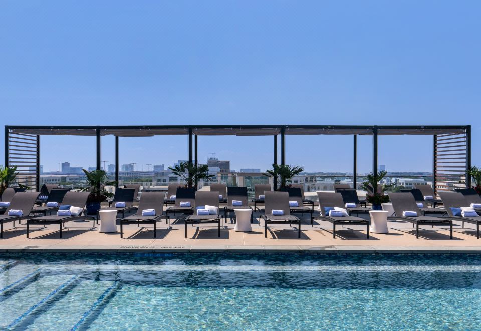 an outdoor pool surrounded by lounge chairs and a dining table , providing a relaxing atmosphere at Omni Frisco at the Star