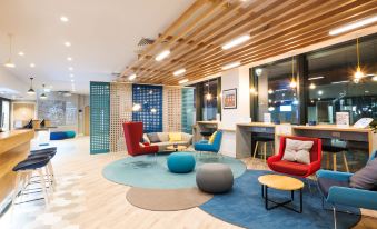 a modern office space with a round rug , red chairs , and various seating options arranged around a coffee table at Holiday Inn Express Stockport