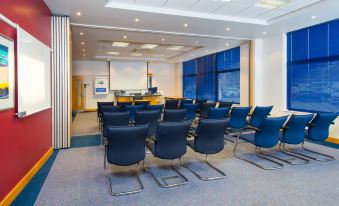 a conference room with blue chairs arranged in rows and a projector screen on the wall at Holiday Inn Express Milton Keynes