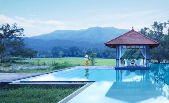 a large , clear swimming pool surrounded by lush green grass and mountains in the background at Jetwing Kaduruketha