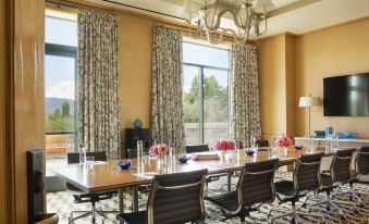 a long wooden table with chairs and a centerpiece of flowers is set up in front of large windows at Rosewood Sand Hill