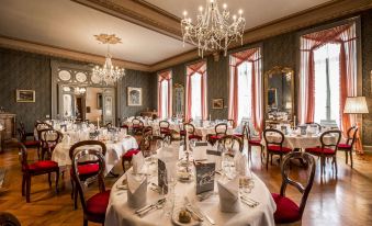 a large , ornate dining room with multiple tables set for a formal dinner , including white tablecloths , wine glasses , and cutlery at Grandhotel Giessbach