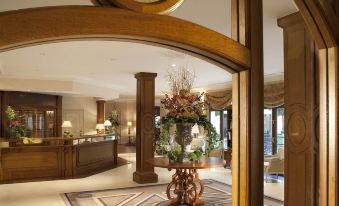 a well - decorated hotel lobby with a wooden reception desk , a potted plant on the floor , and a large clock on the wall at Auberge du Jeu de Paume