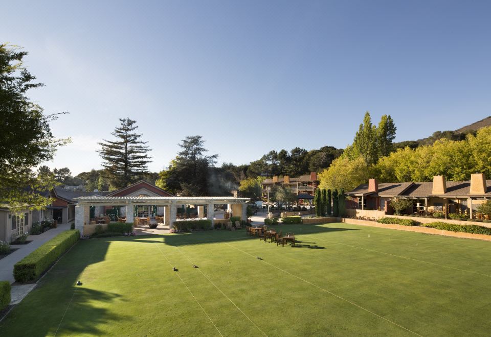 a large , well - maintained green lawn with a few people and buildings in the background , under a clear blue sky at Bernardus Lodge & Spa