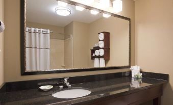a bathroom with a black countertop , white sink , and towels hanging on the wall , reflecting in a large mirror above the sink at Grandstay Hotel Suites Thief River Falls