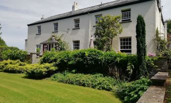 a large white house with green shutters , surrounded by a lush garden and a well - maintained lawn at Buckley Farmhouse
