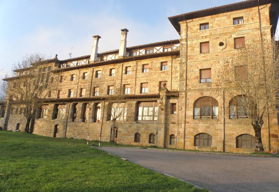 a large stone building with multiple windows and a grassy area in front of it at Balneario de Corconte