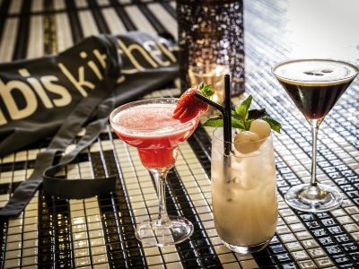 a table with a bar in the background and two cocktails in front of it at Ibis Melbourne Hotel and Apartments