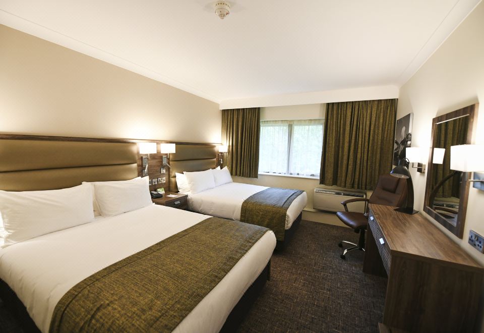 a hotel room with two beds , a desk , and a window , giving it a cozy and comfortable atmosphere at Holiday Inn Telford - Ironbridge