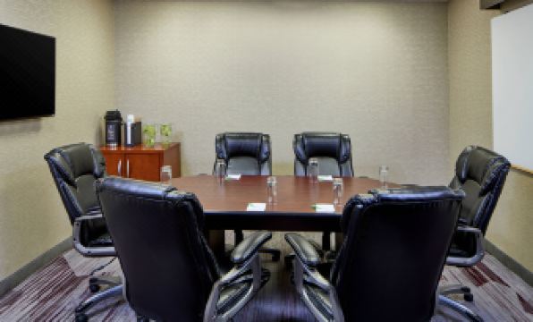 a conference room with a wooden table surrounded by black chairs and two white round tables at Sonesta Select Raleigh Durham Airport Morrisville