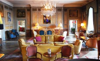 a luxurious living room with yellow sofas , red and white pillows , and a chandelier hanging from the ceiling at Häringe Slott