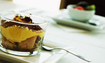 a glass of dessert is placed on a white plate with a spoon , and the dish is filled with yellow cream at Best Western Palace Inn Hotel