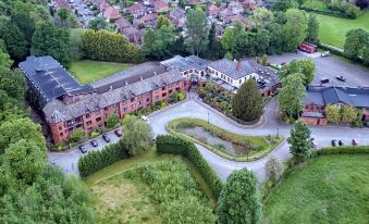 aerial view of a red brick building surrounded by greenery , with cars parked in front of it at Bredbury Hall Hotel