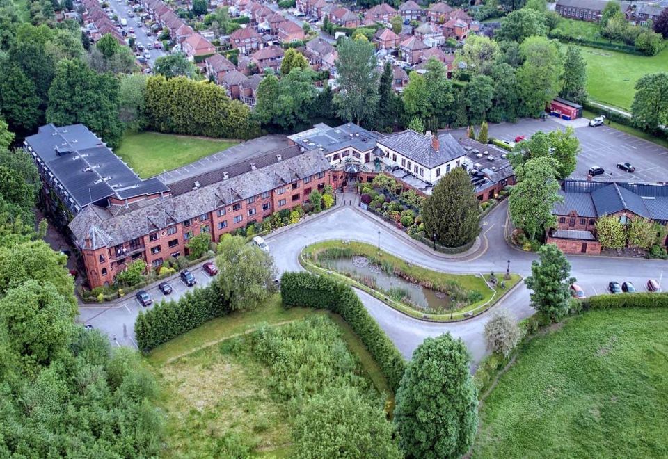 aerial view of a red brick building surrounded by greenery , with cars parked in front of it at Bredbury Hall Hotel