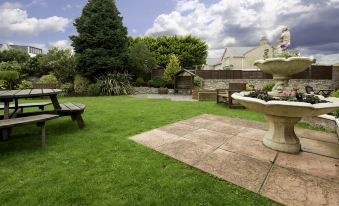 a lush green lawn with a fountain in the middle , surrounded by a wooden fence at Best Western Weymouth Hotel Rembrandt