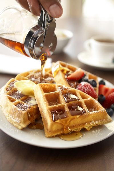 a plate of waffles with syrup being poured over , accompanied by a cup of coffee at Country Inn & Suites by Radisson, Watertown, SD