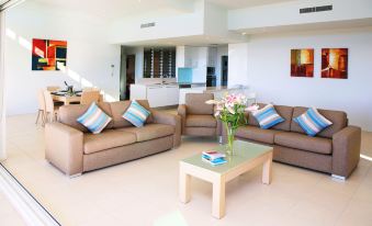 a spacious living room with two brown couches , a dining table , and a kitchen in the background at Akama Resort