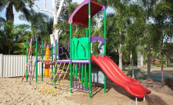 a colorful playground with various play equipment , including a slide , swings , and a jungle gym , surrounded by palm trees at Discovery Parks - Rockhampton