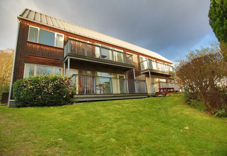 a large wooden house with a balcony and green lawn , surrounded by trees and grass at Best Western Plus Oaklands Hotel