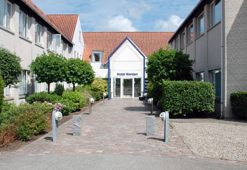 a brick building with a blue door is surrounded by trees and bushes , with a gravel driveway leading up to it at Hotel Norden