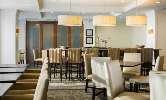 a restaurant with various seating options , including chairs and tables , under pendant lights hanging from the ceiling at Hampton Inn Hallandale Beach-Aventura