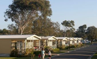 a row of houses with white roofs , surrounded by trees and people walking on the street at Beachfront Hallidays Point