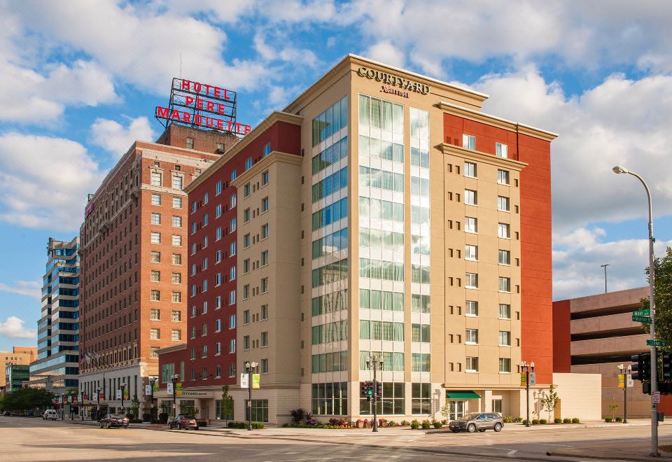 a modern hotel building with multiple floors , surrounded by cars and a clear blue sky at Courtyard Peoria Downtown