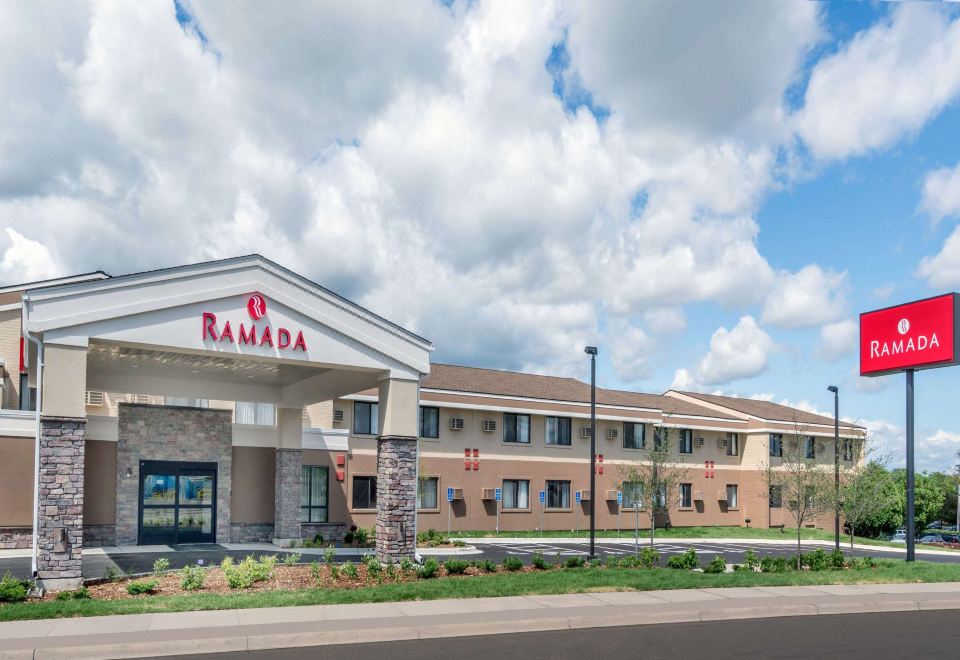 a large hotel with a red and white sign on the front , located in a city setting at Ramada by Wyndham Minneapolis Golden Valley